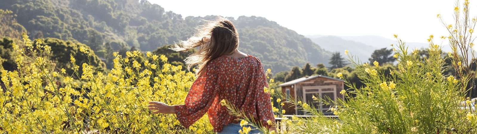 woman from behind wearing a flowery blouse looking over the yellow field of flowers among the valley of Carmel Valley resort