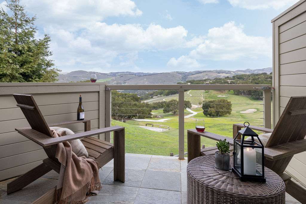 A balcony with a deck chair and glasses of wine looking out to a view of Carmel Valley