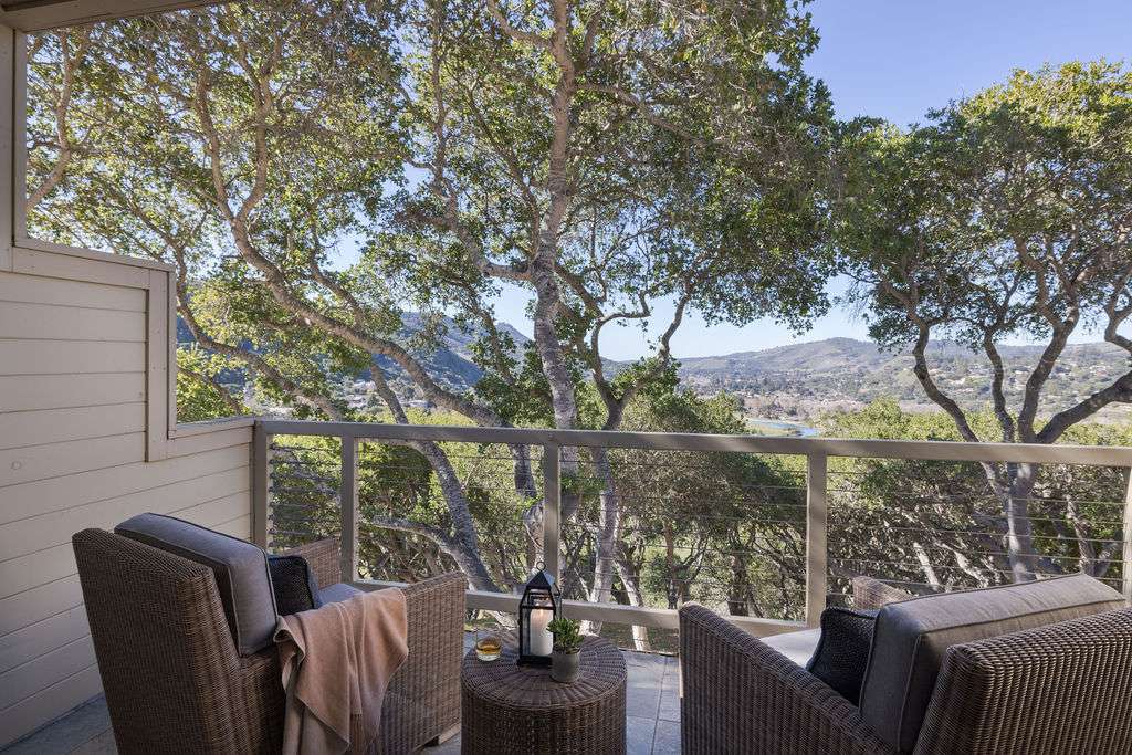 A balcony with two armchairs and a view of large trees