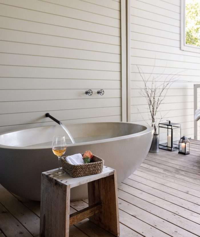 A balcony with an outdoor tub and table set with a glass of wine