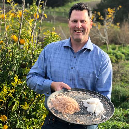 photo of Carlo Overhulser, a man who professionally harvests salt for Carmel Valley ranch, smiling at camera and holding a big black plate with two types of salts