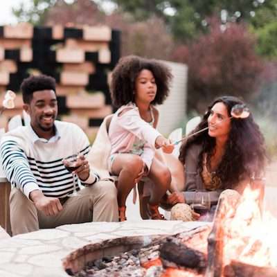 Family of four roasting marshmallows over a stone firepit