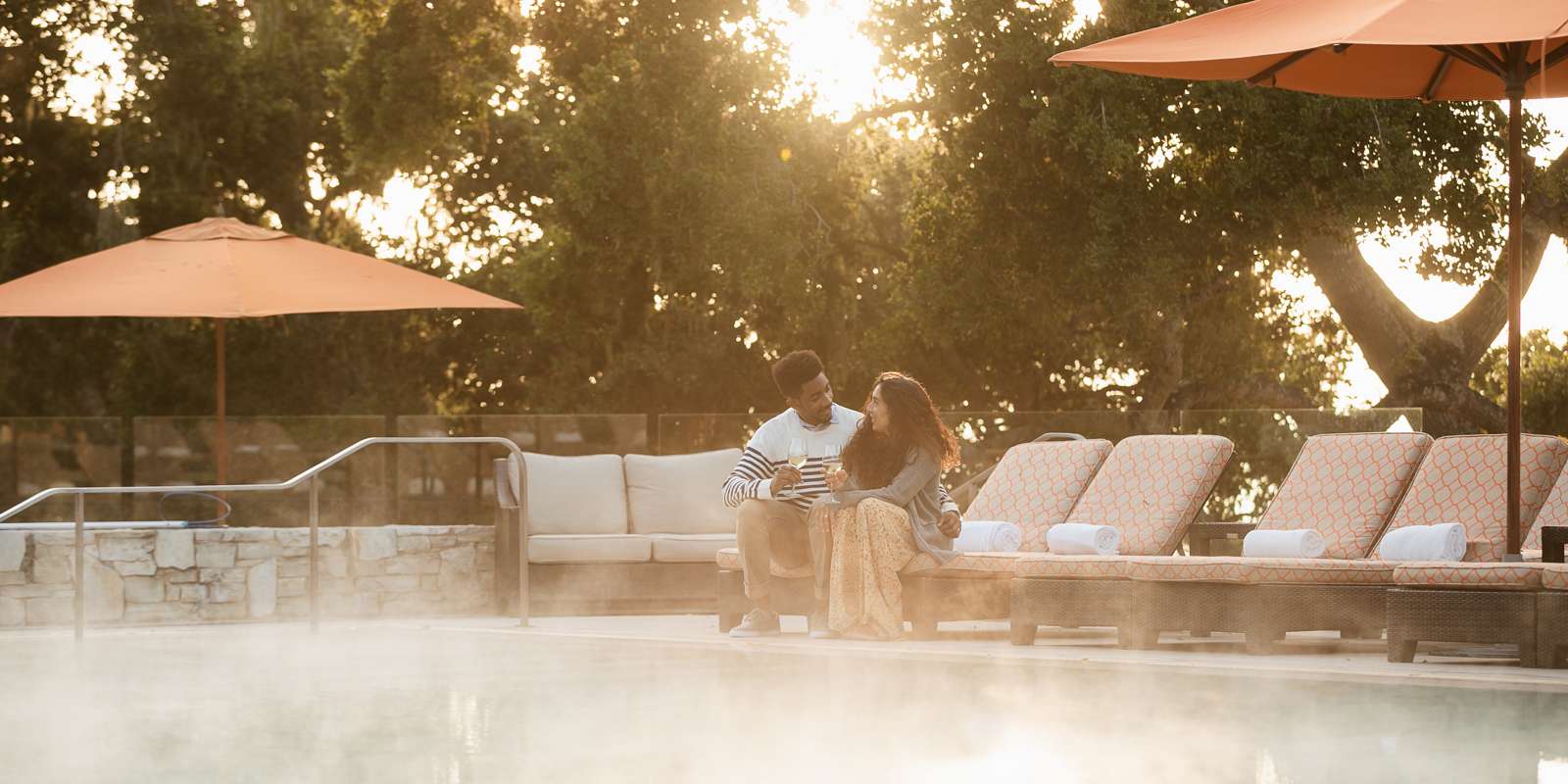 Couple sitting on lounge chair at pool having a glass of wine