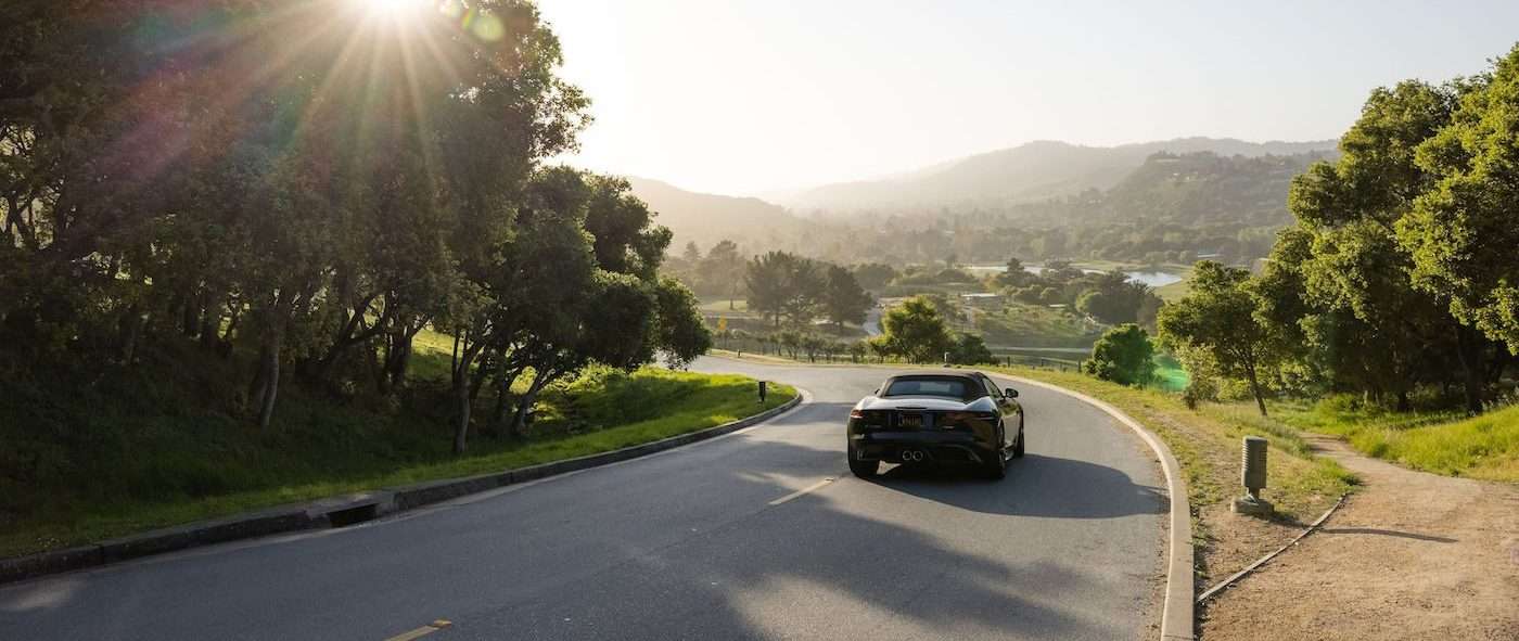 a black car going down a beautiful road surrounded by green trees and valleys at Carmel