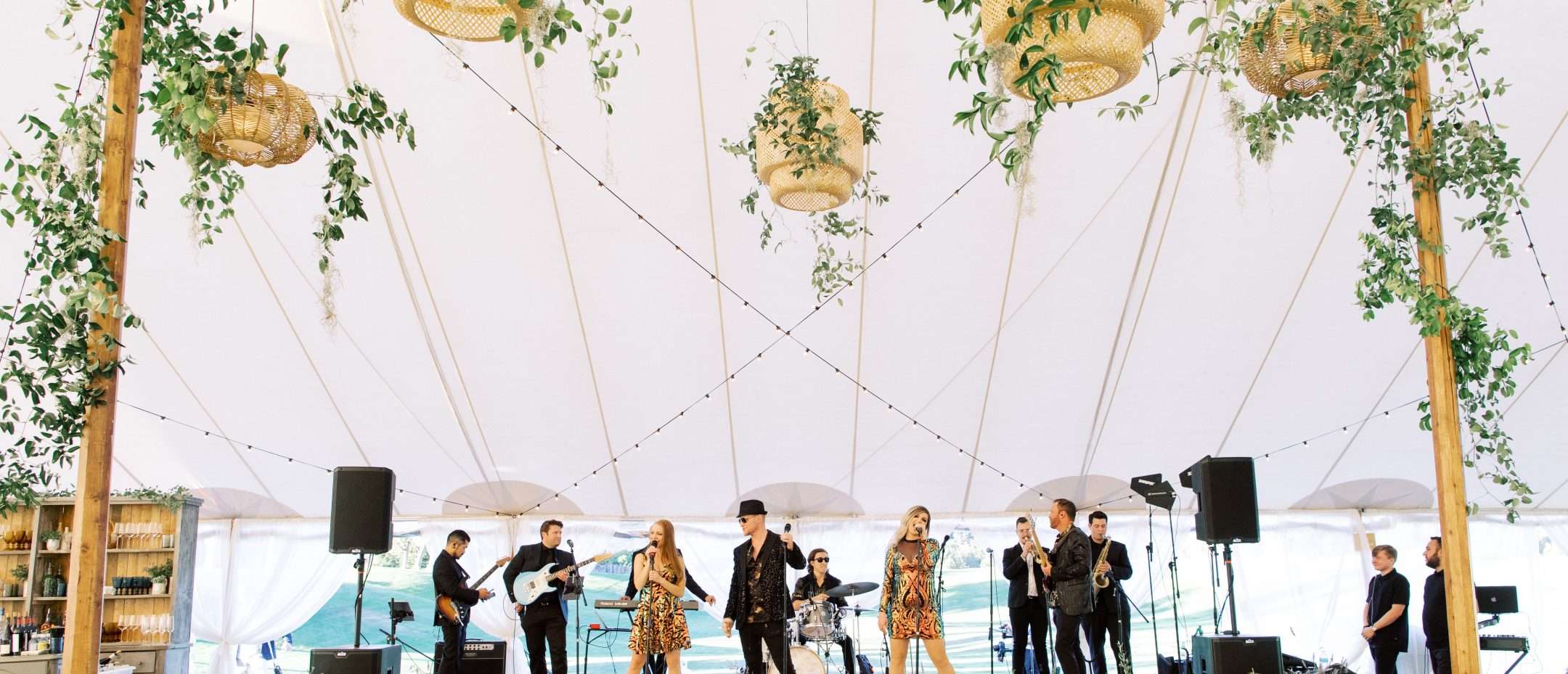Band on stage under white tent with hanging baskets of greenery